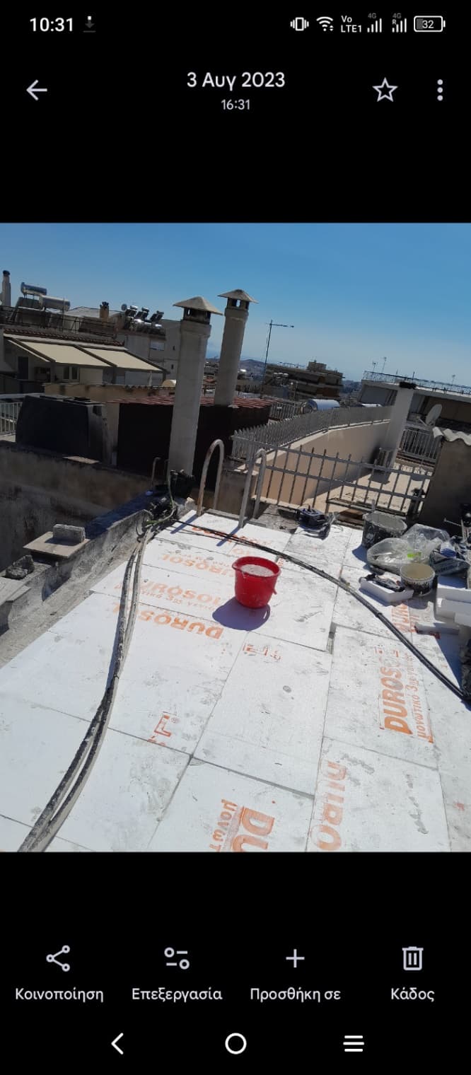 Rooftop construction site with insulation boards labeled Durosol, a red bucket in the center, and various construction materials scattered around under a clear blue sky