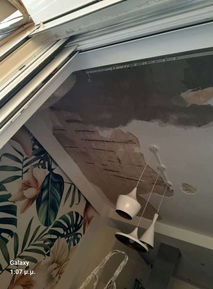 Interior view of a room with ceiling damage, hanging white pendant lights, a floral and leaf wall mural, and a ladder