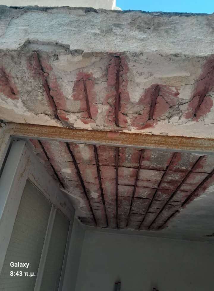 Interior view of a building ceiling with visible damage, showing rusted rebar and deteriorated concrete layers